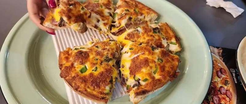 نمای نزدیک از پیتزا پر پنیر و خوشمزه رستوران پیتزا سه فر، با کراست طلایی و کش آمدن پنیر داغ در یک بشقاب سبز.