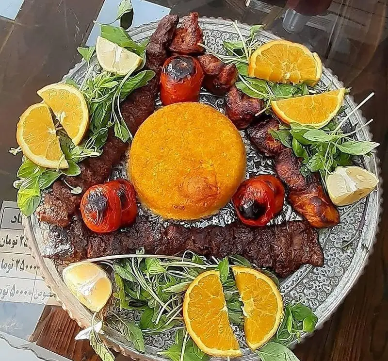 کته کباب سجاد: یک دیس خوشمزه کته کباب سنتی ایرانی با ته دیگ طلایی، کباب آبدار، گوجه کبابی، پرتقال و سبزی تازه.