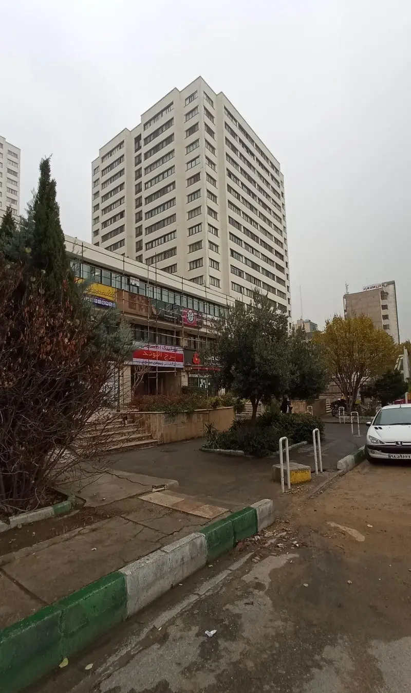 تصویر ساختمان بلند "برج الوند" با نمای تجاری، شامل تابلوی "وارطان لند" در طبقات پایینی. نمایی از یک کسب و کار شهری.