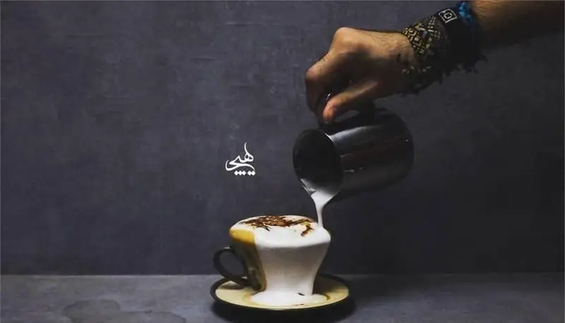 یک باریستا در حال ریختن شیر فوم‌دار و غلیظ روی قهوه، منظره‌ای هنری از لاته یا کاپوچینو در کافی شاپ هیچ. تجربه طعم بی‌نظیر.