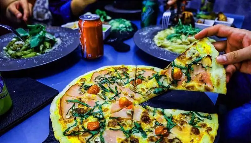 میز پر از غذای لذیذ در کافی شاپ هیچ: پیتزای تازه با پاستا و نوشیدنی. لذت دورهمی و صرف یک وعده خوشمزه در کافه هیچ.