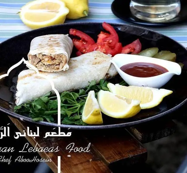 تصویری از شاورما لذیذ لبنانی رستوران الریان. شامل رول‌های گوشت یا مرغ با سس مخصوص، لیمو، گوجه و سبزیجات تازه.