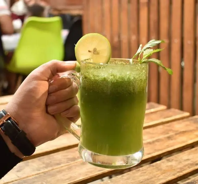 نوشیدنی سبز خنک و تازه (موهیتو یا لیموناد نعنا) با تزئین لیمو و برگ نعنا در رستوران لبنانی الریعان، انتخابی عالی برای طراوت.