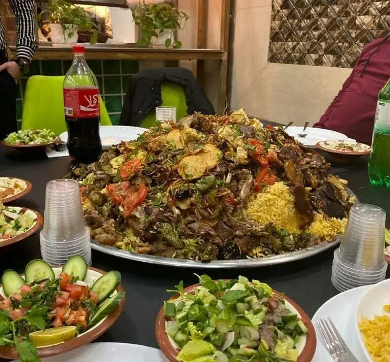 یک میز شام مفصل و پر از غذای لذیذ در رستوران لبنانی الریعان، شامل دیس بزرگ پلو با گوشت بره و سبزیجات، سالادهای تازه و نوشیدنی‌های خنک برای تجربه طعم اصیل لبنانی