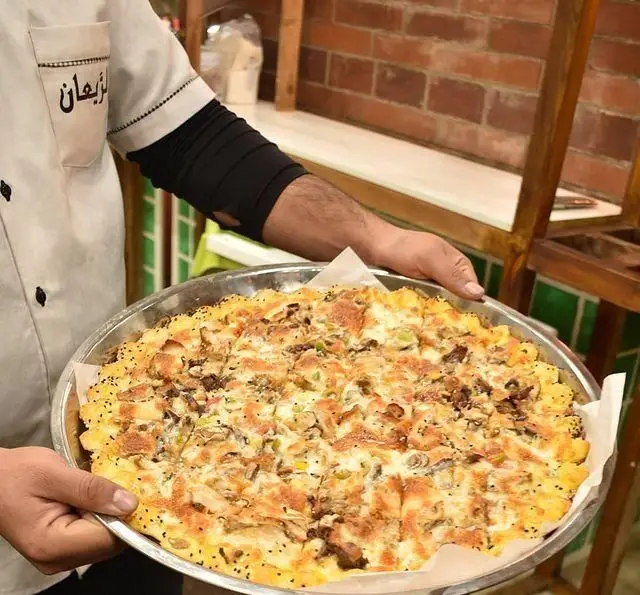سرو پیتزای مرغ و قارچ داغ و خوشمزه رستوران لبنانی الریعان توسط پرسنل. بهترین پیتزا و غذاهای سنتی لبنانی.
