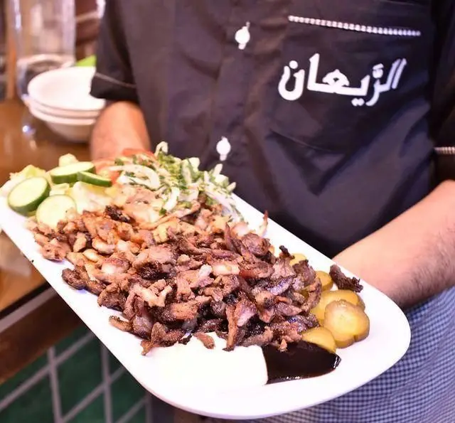 پرسنل رستوران لبنانی الریعان در حال سرو بشقاب بزرگ شاورما یا گوشت کبابی خوشمزه با سالاد، خیار و ترشی برای مشتریان.