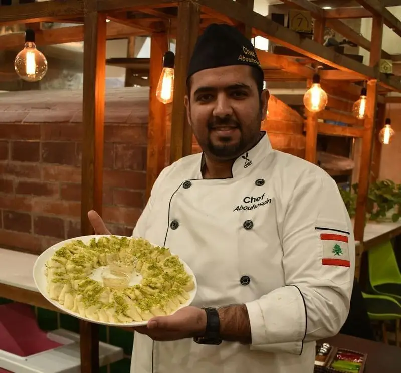 سرآشپز ابوحسین از رستوران لبنانی الریعان، دسر سنتی و زیبای لبنانی را با پسته و طعم بی‌نظیر برای مهمانان سرو می‌کند.