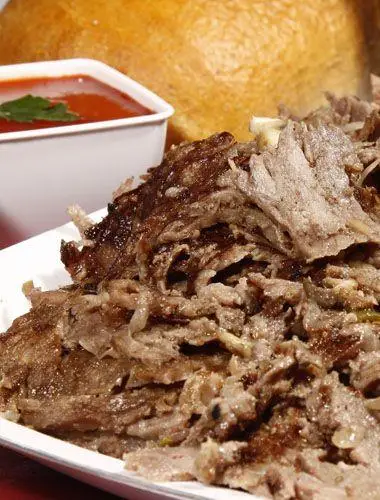 تصویری از ساندویچ دونر کباب ترکی لذیذ و پرملات ساندویچی نشاط با برش‌های گوشت گریل شده، سس قرمز ویژه و نان تازه در پس‌زمینه.