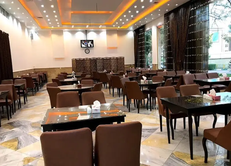 نمای داخلی وسیع کافه رستوران فارسی با دکوراسیون مدرن، نورپردازی دلنشین، چیدمان منظم میز و صندلی‌ها، آماده پذیرایی از مشتریان.