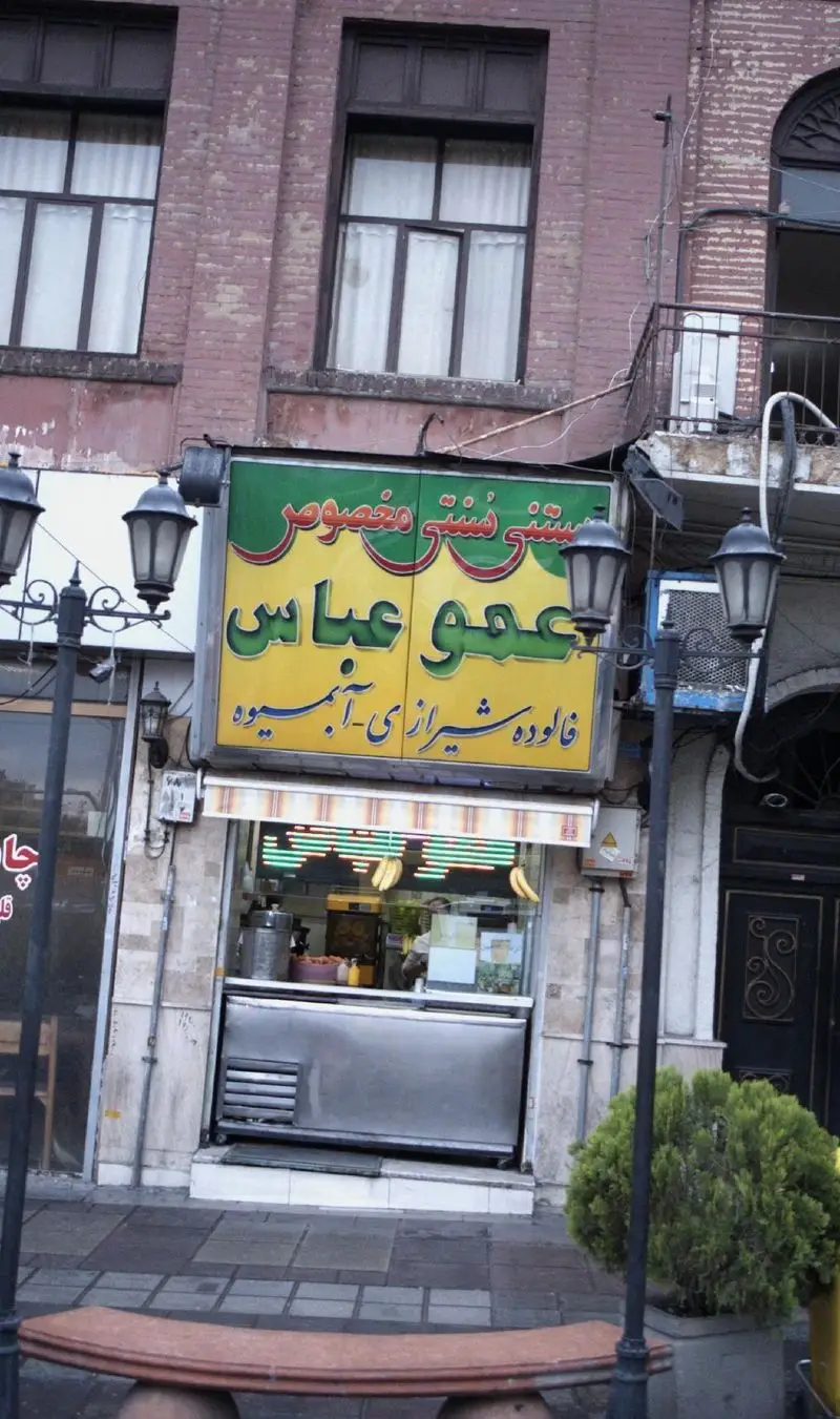 کسب و کار عمو عباس، مغازه بستنی و فالوده مخصوص و آبمیوه شیرازی با تابلوی زرد و سبز در نمای ساختمان آجری.