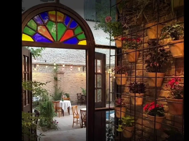 کافه کتاب نیکو: فضای باز سنتی با پنجره ارسی رنگارنگ، حیاط دنج و دیوار سبز گلدانی، مکانی ایده آل برای مطالعه و دورهمی.