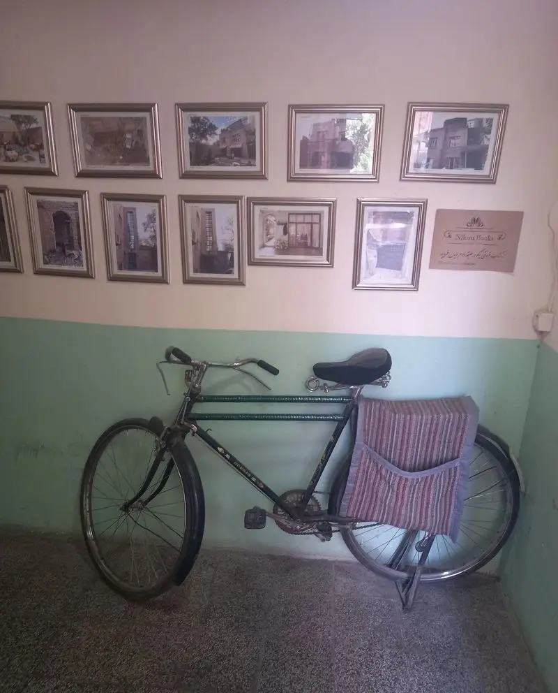 دوچرخه کلاسیک در کافه کتاب نیکو، دیواری با مجموعه‌ای از قاب‌های هنری از معماری، فضایی دنج و الهام‌بخش برای مطالعه و گفتگو