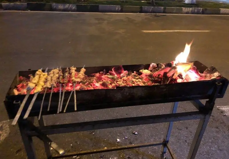 کباب‌های خوش‌طعم جگر و دل و قلوه روی سیخ‌های فلزی در حال کباب شدن بر روی زغال‌های گداخته و آتش در فضای شب جگرسرای کلاسیک.