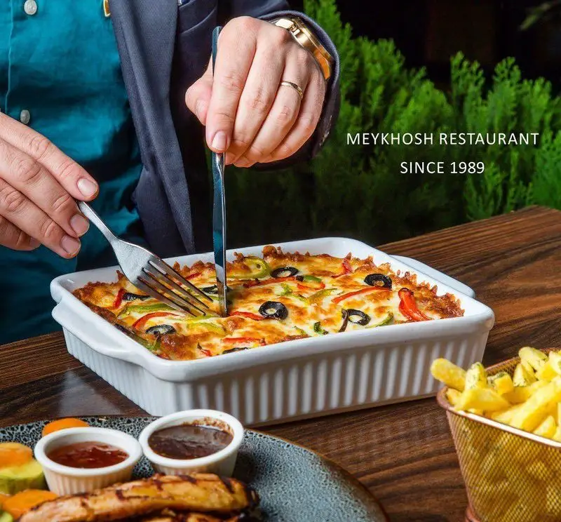 رستوران میخوش: مشتری در حال برش یک لازانیا/خوراک پنیری داغ و خوشمزه با فلفل و زیتون. بهترین گزینه برای پیتزا و غذای فرنگی در تهران.