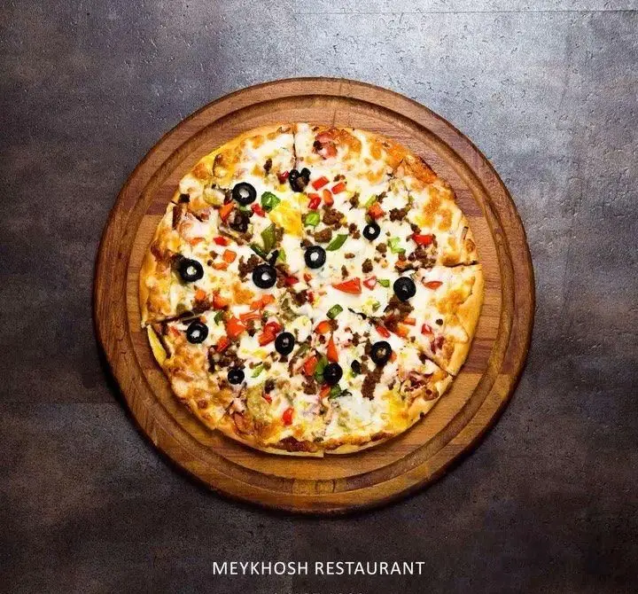 عکس پیتزا مخصوص رستوران میخوش با تاپینگ متنوع زیتون، گوشت و فلفل دلمه‌ای، سرو شده روی تخته چوبی.
