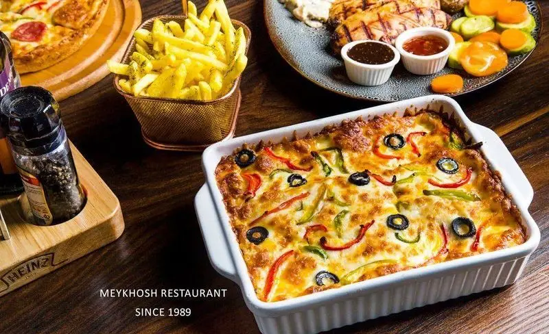 نمای جذاب از غذاهای لذیذ رستوران میخوش شامل پاستا پخته شده، سیب زمینی سرخ کرده و کباب. بهترین پیتزا و غذاهای ایرانی با کیفیت.