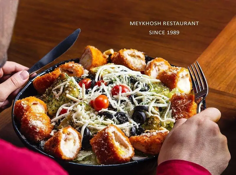 نمایی نزدیک از سالاد مجلل رستوران میخوش با مرغ سوخاری، پنیر فراوان و سبزیجات تازه برای یک وعده غذایی لذت‌بخش.