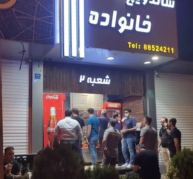 ساندویچ خانواده شعبه ۲ در شب، مملو از مشتریان که برای فست فودهای محبوب و ساندویچ‌های خوشمزه سفارش می‌دهند. تلفن: 88524211