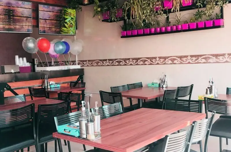 فضای داخلی فست فود ریحانه با دکوراسیونی جذاب و مدرن، میز و صندلی‌های مرتب، بادکنک‌های شاد و گلدان‌های آویز صورتی.