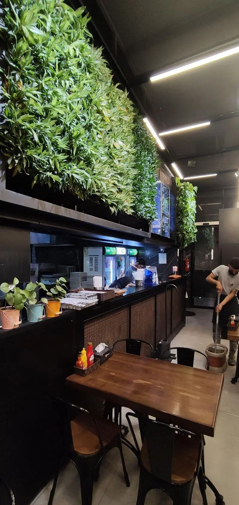 فضای داخلی جذاب و مدرن فست فود شیلا شعبه دولت، شامل دیوار سبز چشم‌نواز، میز و صندلی‌های شیک و محیطی تمیز برای مشتریان.