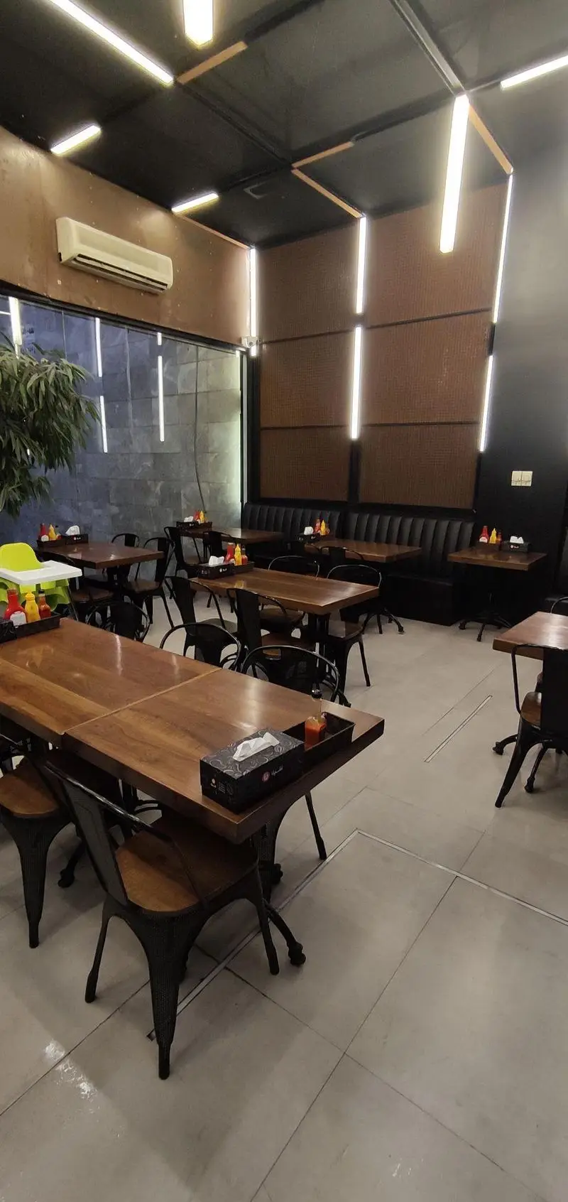 فضای داخلی مدرن و دنج فست فود شیلا شعبه دولت با میز و صندلی‌های چوبی، نورپردازی خاص و دیوارهای شیک، آماده پذیرایی.