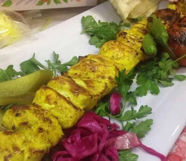 یک سیخ جوجه کباب زعفرانی طلایی و لذیذ با فلفل و گوجه کبابی، ترشی کلم و خیارشور در رستوران ایرانیان.