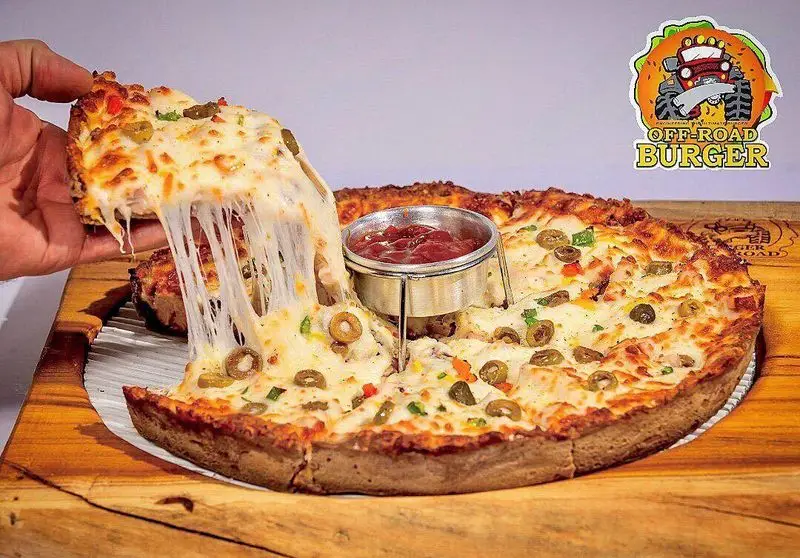 تصویری از یک پیتزای ویژه و خوشمزه با کش پنیر فوق‌العاده در منوی آفرود گریل، همراه با سس و تاپینگ زیتون و فلفل.