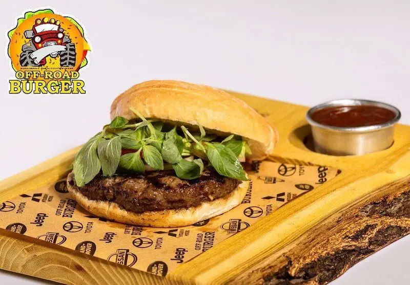 برگر گوشت تازه آفرود گریل با نان خاص و سبزیجات معطر روی تخته سرو چوبی. مناسب برای منوی رستوران آفرود برگر.