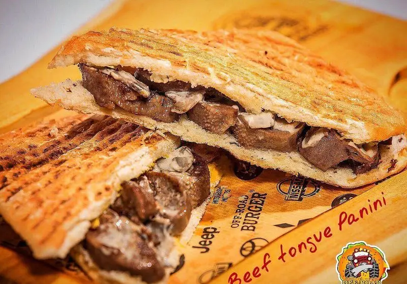 ساندویچ پانینی زبان گوساله خوشمزه آفرود گریل، با نان تست شده و محتویات لذیذ، تصویری جذاب از منوی رستوران Off-Road Burger.