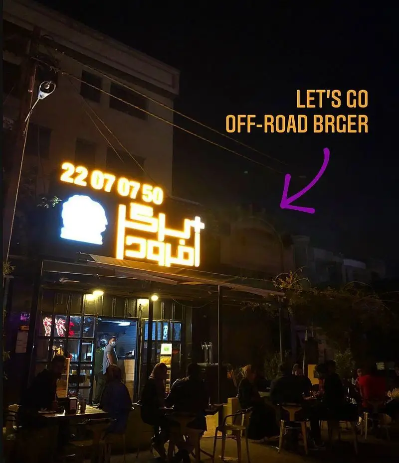 آفرود برگر، نمای شبانه رستورانی شیک با تابلوی نئونی درخشان و شماره تماس ۲۲۰۷۰۷۵۰، پذیرایی از مشتریان در فضای باز.