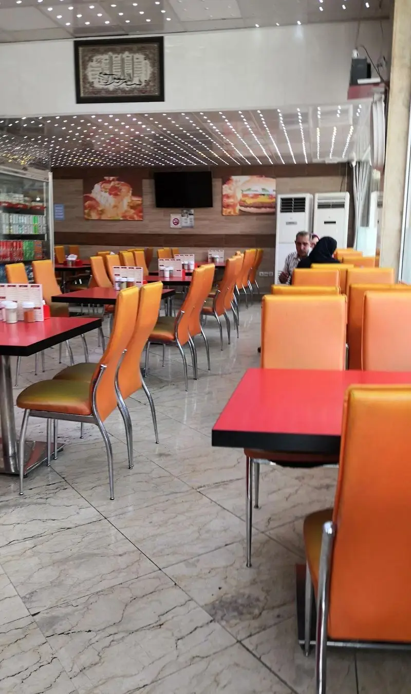 محیط دلنشین و تمیز فست فود باران، با دکوراسیون داخلی مدرن، میز و صندلی‌های راحت نارنجی و تابلوهای اشتهابرانگیز غذا.