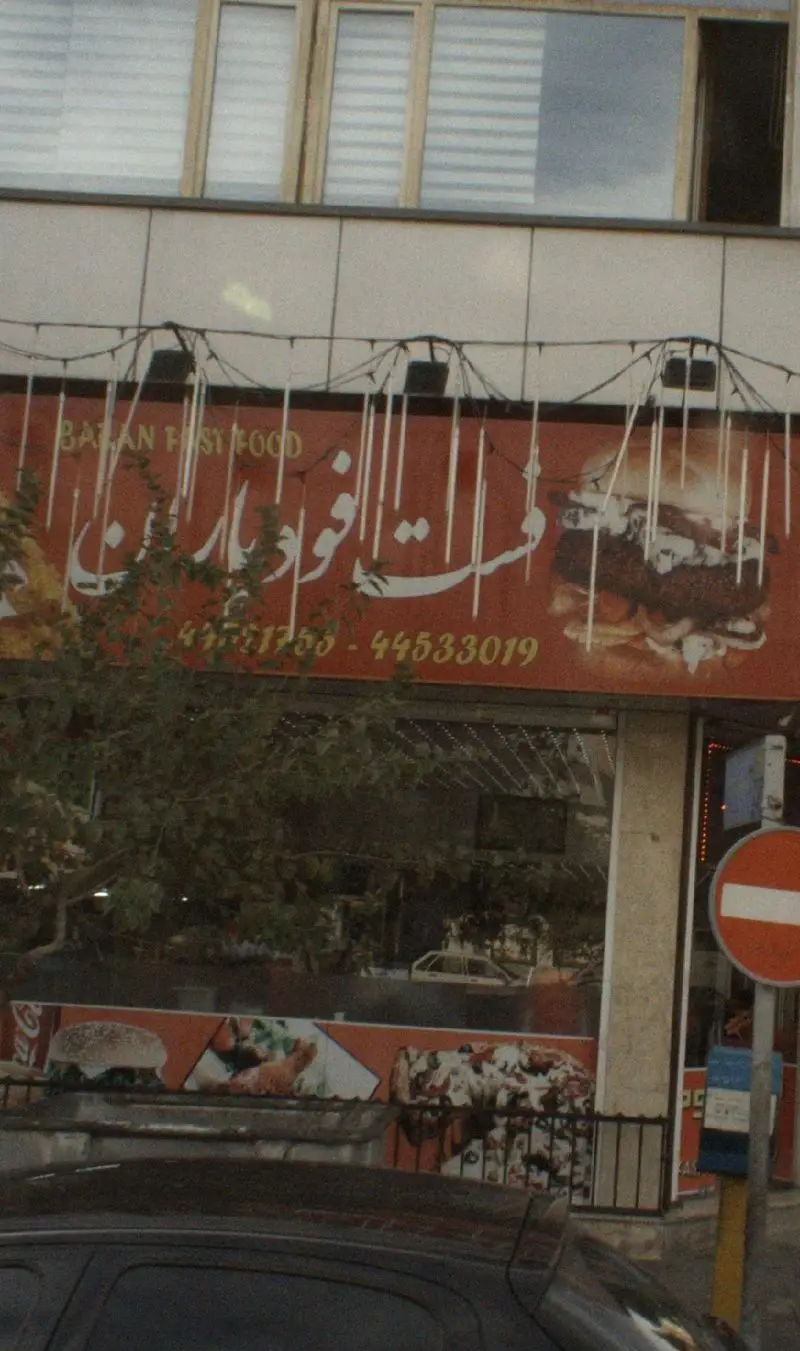 تابلوی فست فود باران با لوگوی بزرگ همبرگر، پیتزا و مرغ سوخاری. شماره تلفن‌های 4351753 و 44533019. بهترین فست فود منطقه.