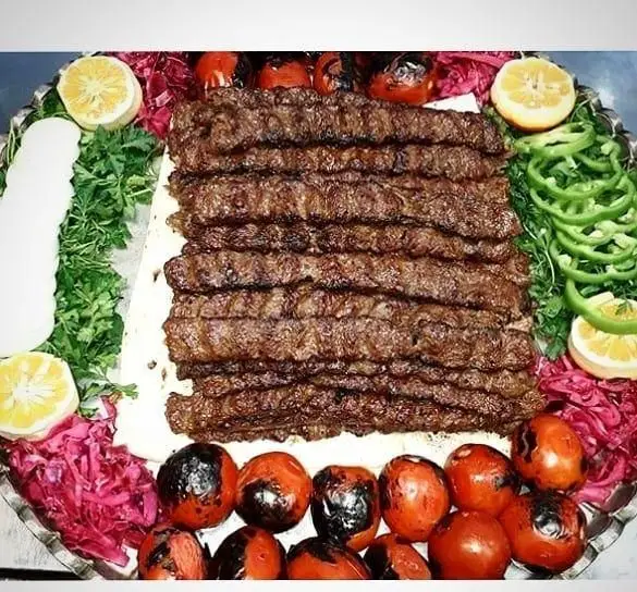 یک سینی بزرگ کباب کوبیده اصیل و مجلسی کترینگ و غذای ایرانی پارسا، سرو شده با گوجه کبابی، سبزیجات تازه، فلفل، لیمو و نان.