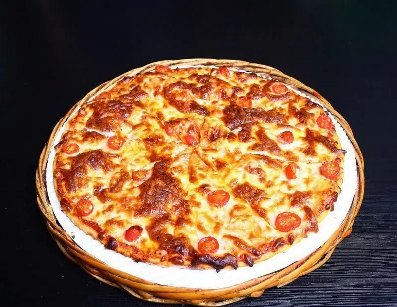 یک پیتزای کامل و داغ با پنیر طلایی ذوب شده و گوجه گیلاسی تازه، از منوی رستوران ایتالیایی ژولی. لذت یک غذای ایتالیایی اصیل.