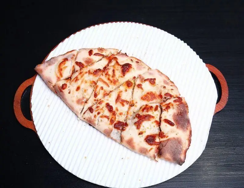 پیتزا پنیری تازه و خوشمزه رستوران ایتالیایی ژولی، برش خورده روی سینی سفید آماده سرو، تجربه‌ای دلپذیر از طعم اصیل ایتالیا.