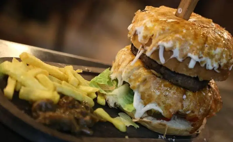 تصویری از یک برگر دوبل لذیذ و پرپنیر با سیب زمینی سرخ کرده و سس مخصوص در رستوران ایتالیایی ژولی، انتخابی ایده‌آل برای یک وعده غذایی دلچسب.