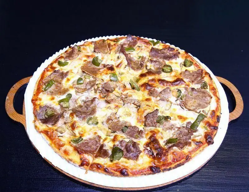 پیتزا گوشت و فلفل سبز داغ و لذیذ رستوران ایتالیایی ژولی با پنیر موزارلای آب شده، آماده در یک سینی چوبی زیبا و سنتی.