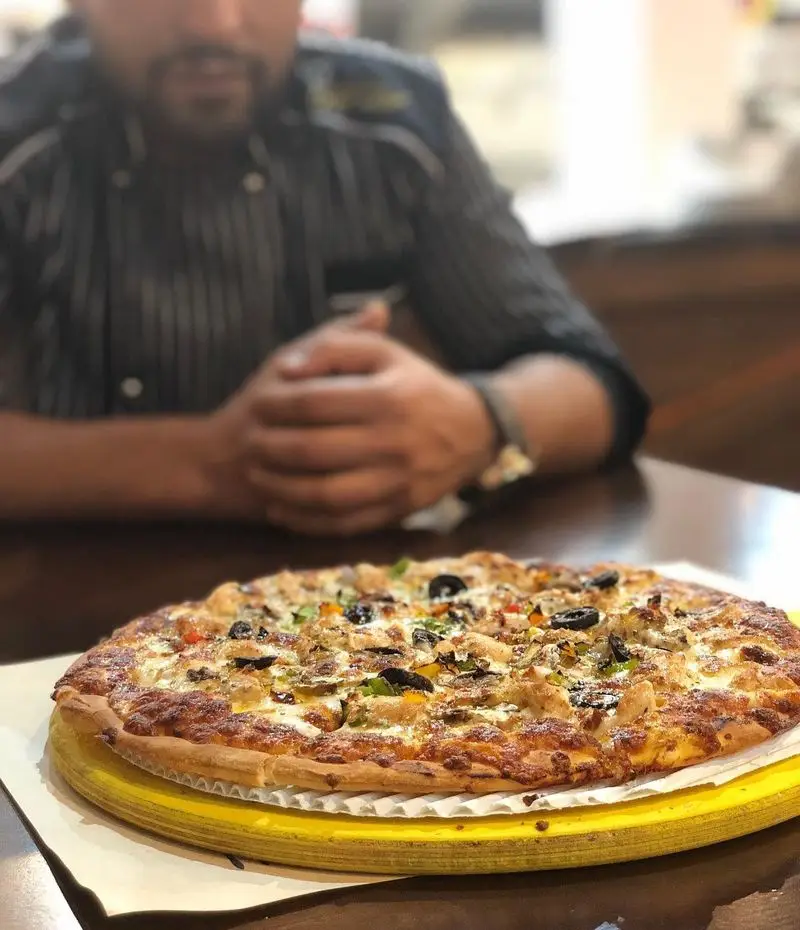 یک پیتزای خوشمزه و داغ مرغ و زیتون در رستوران ایتالیایی ژولی، با پنیر فراوان و فلفل دلمه‌ای، آماده سرو برای مشتریان.