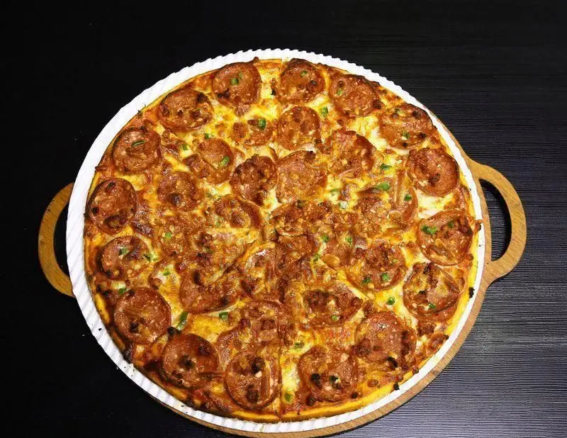 پیتزا پپرونی و سوسیس مخصوص رستوران ایتالیایی ژولی، با پنیر فراوان و گوشت‌های ترد، آماده سرو روی تخته چوبی، طعم بی‌نظیر ایتالیایی.