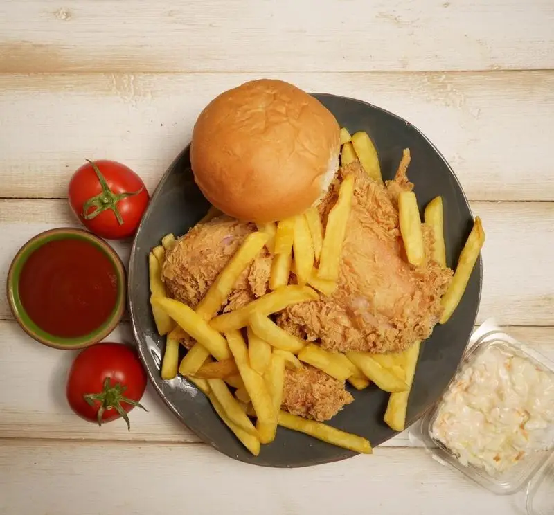 وعده غذایی کامل و خوشمزه از فست فود ریحان: مرغ سوخاری ترد، سیب زمینی سرخ کرده طلایی، نان برگر، سس کچاپ و سالاد کلم تازه.