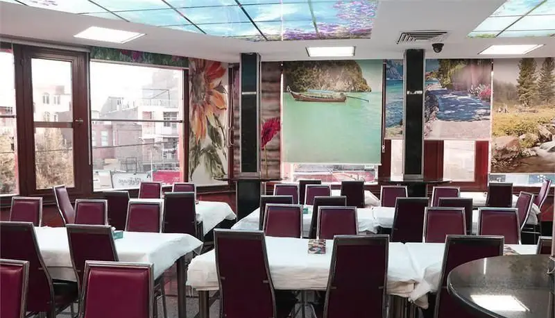 محیط داخلی فست فود اغذیه نشاط با میز و صندلی‌های چیده شده، دکوراسیون دیواری جذاب و سقف نورانی، آماده پذیرایی از مشتریان.