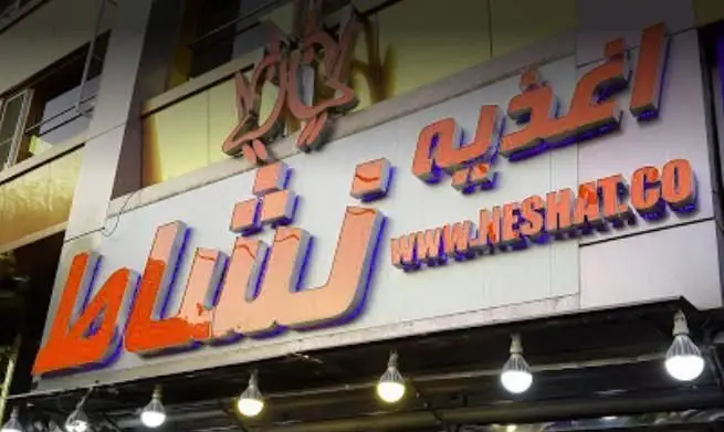 تابلو سردر فست فود اغذیه نشاط با حروف نارنجی برجسته، شامل لوگو و آدرس وبسایت www.neshat.co در شب.