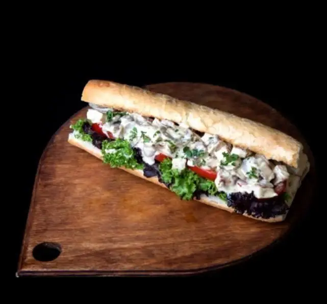 ساندویچ خوشمزه فست فود هات باکس با مواد تازه و سس مخصوص، نان باگت طلایی روی تخته چوبی برای مشتریان هات باکس