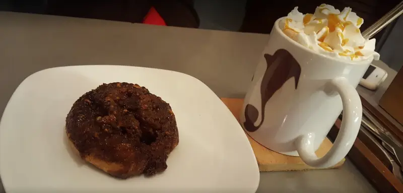 یک شیرینی دارچینی با مغز و سس کارامل همراه با ماگ نوشیدنی خامه دار از کافه رئیس، تجربه شیرین در یک کافه‌گردی