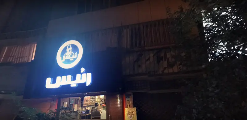 سردر نورانی کافه رئیس در شب، نمایشگر لوگو و نام برند. مکانی دنج و دلنشین برای صرف قهوه و انواع نوشیدنی‌های گرم و سرد.