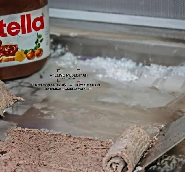 تهیه بستنی رولی نوتلا تازه در کافه بستنی نیترولی، با قوطی نوتلا و اسپاچول بر روی صفحه سرد برای دسری خوشمزه.