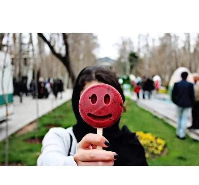 یک چوب بستنی یخی خندان و قرمز رنگ میوه‌ای در دست فردی، دسر سرد و خوشمزه‌ای از کافه بستنی نیترولی.