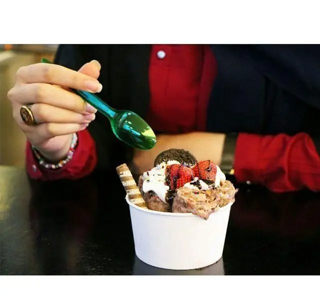 دست مشتری در حال برداشتن قاشقی از بستنی رول توت فرنگی و اورئو کافه بستنی نیترولی؛ دسر خوشمزه و جذاب برای تجربه ای شیرین.