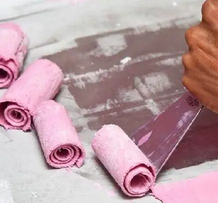 تصویری جذاب از مراحل تهیه و رول کردن بستنی صورتی در کافه بستنی نیترولی، نشان دهنده کیفیت و تازگی محصول.