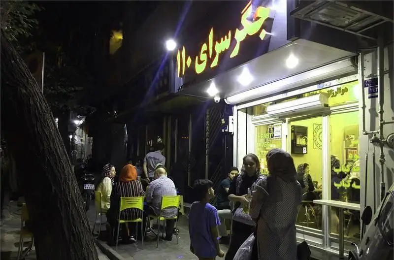 تصویری از جگر سرای ۱۱۰ در شب با مشتریان نشسته در فضای باز، ارائه دهنده بهترین جگر کبابی و غذای ایرانی.
